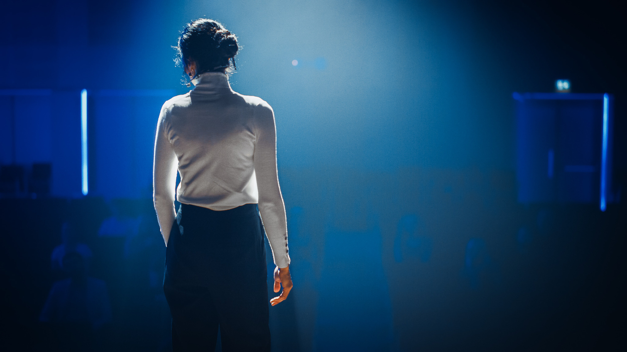 Female Motivational Speaker on Stage, Talking about Happiness, Diversity, Success, Leadership, STEM and How to Be Productive. Woman Presenter Leads Tech Business Conference. Back View Shot